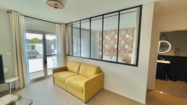 A modern living room with a yellow sofa, a large window with a view, and a mirrored wall. - The Originals City, Ara Hotel, Landerneau (Landerneau)