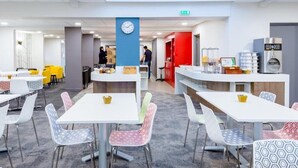 A modern cafeteria with white tables and colorful chairs, a clock on the wall, and a coffee machine. - The Originals City, Ara Hotel, Landerneau (Landerneau)