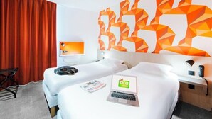 A hotel room with two beds, a desk, a chair, a laptop, and a wall with geometric orange patterns. - The Originals City, Ara Hotel, Landerneau (Landerneau)