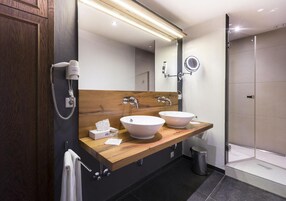 Un baño moderno con dos lavamanos, un mueble de tocador de madera, un espejo grande, un secador de pelo y una cabina de ducha de vidrio.