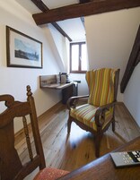 Una habitación acogedora con una silla de madera, un sillón a rayas, una mesa con un control remoto y un cuadro en la pared.