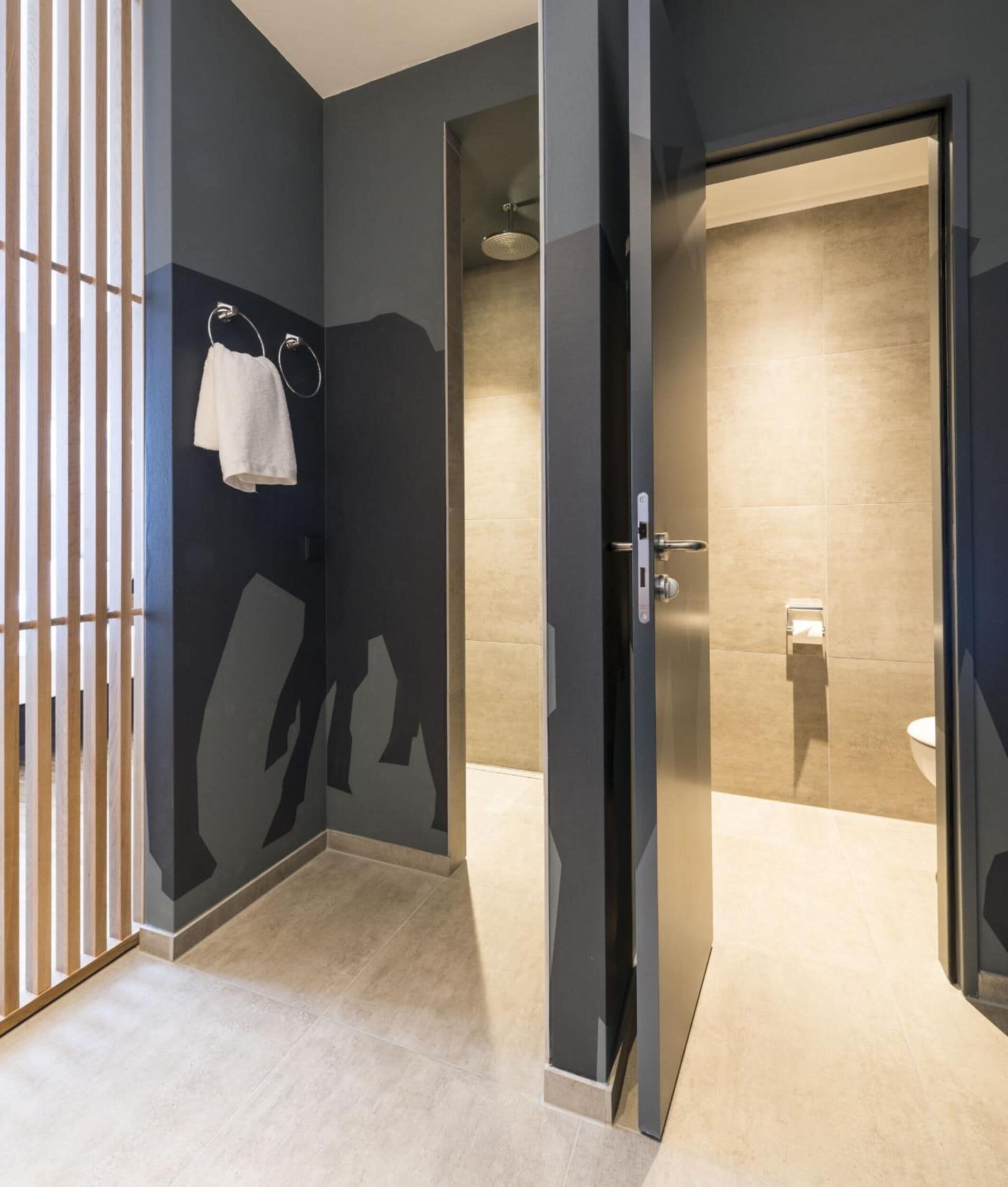 A modern bathroom with a dark wall, a towel rack with a white towel, and a toilet visible through a glass partition.