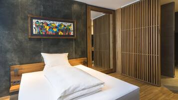 A modern hotel room with a large bed, a wooden headboard, a framed abstract painting, and a sliding wooden door.