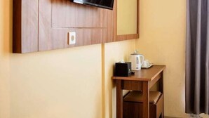 A hotel room with a flat-screen TV mounted on a wooden panel, a small wooden table with a kettle, and a mirror above the TV. - Portola Grand Renggali Hotel (Takengon)