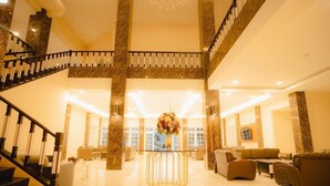 A spacious lobby with a grand staircase, a central round table with a floral arrangement, and comfortable seating areas. - Portola Grand Renggali Hotel (Takengon)