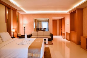 A hotel room with a bed, a sofa, a coffee table, and a mirror. - Portola Grand Renggali Hotel (Takengon)