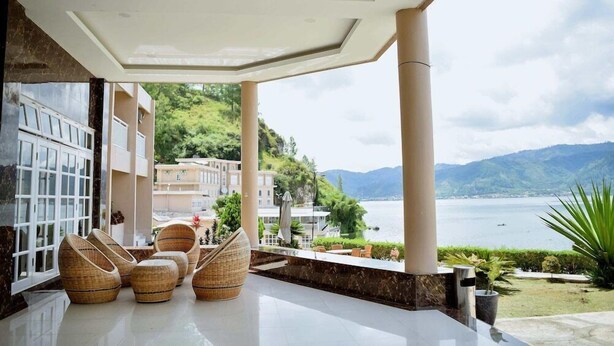A spacious outdoor seating area with wicker chairs and a view of a lake and mountains. - Portola Grand Renggali Hotel (Takengon)