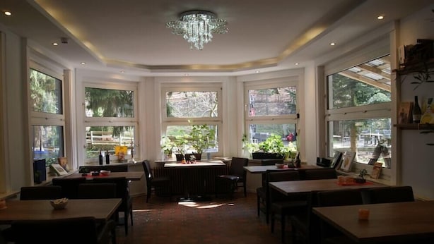 A dining area with tables and chairs, large windows, and a chandelier. - Hotel Radevormwald (Radevormwald)