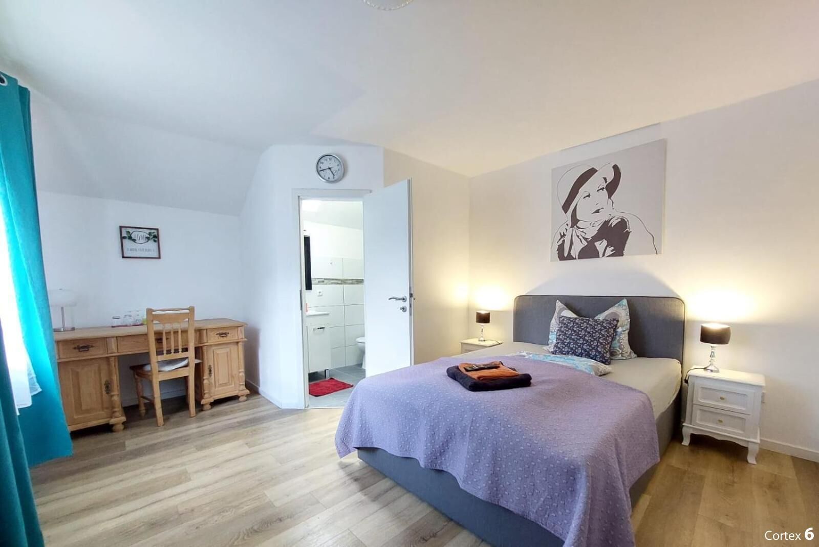 Ein Schlafzimmer mit einem Bett, Nachttischen, einem Schreibtisch und einem Stuhl. Eine Tür führt ins Badezimmer.
