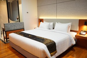 Quarto de hotel com uma cama grande, mesa de cabeceira com abajur, espelho e piso de madeira.