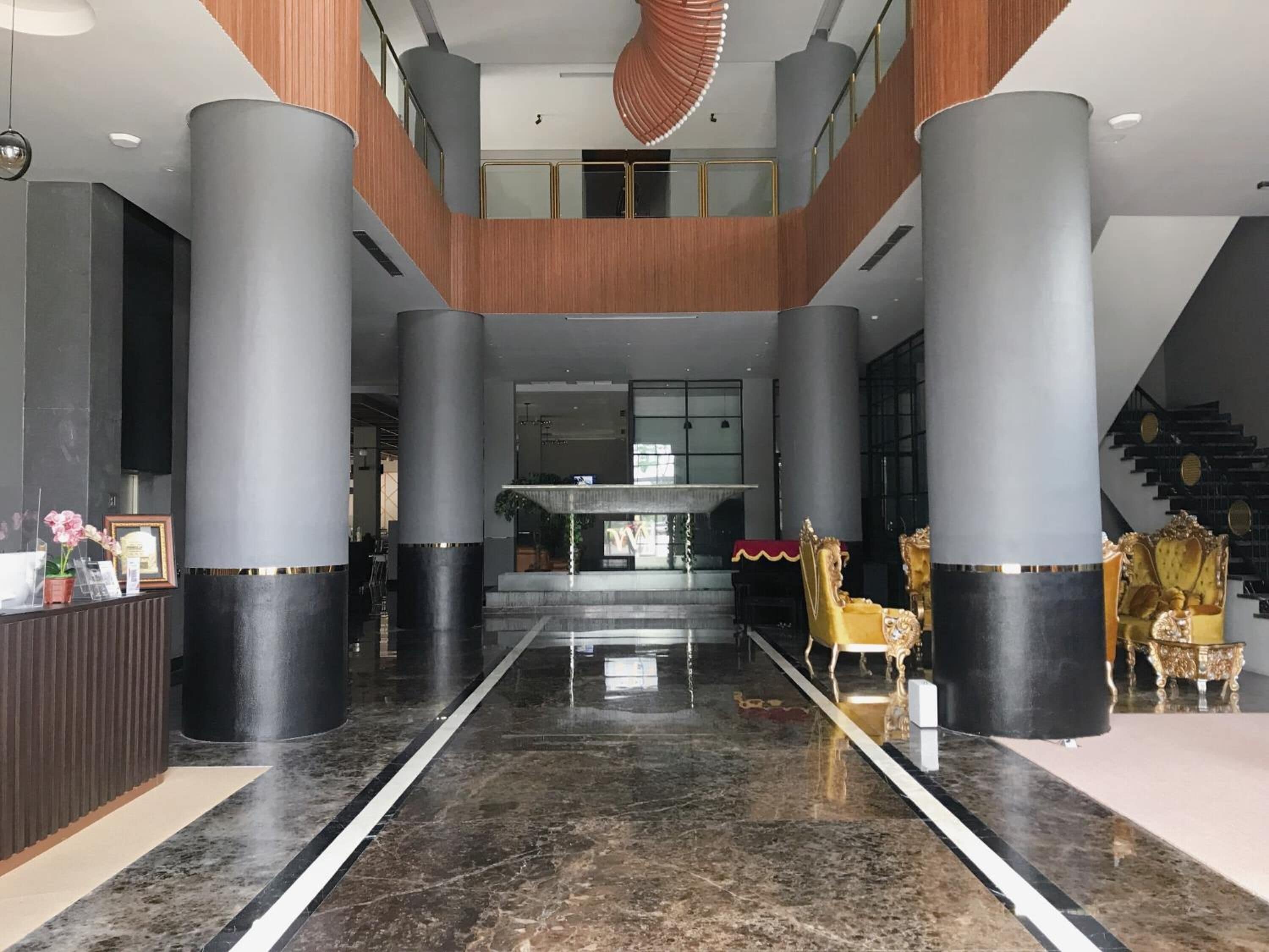 Un hall d’entrée spacieux, doté d’un sol en marbre, de grandes colonnes, d’un comptoir de réception et de fauteuils dorés richement décorés.
