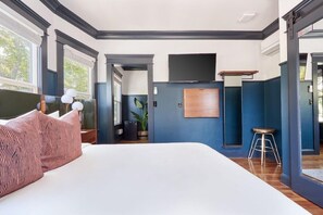 A modern bedroom with a large bed, a TV mounted on the wall, and a small stool. - Sonder The Baker (San Diego)