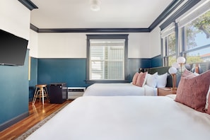 A hotel room with a large bed, a small desk, a chair, a radiator, and a window with blinds. - Sonder The Baker (San Diego)