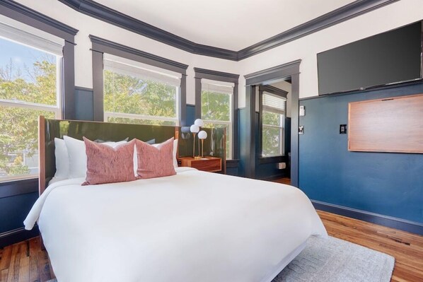 A bedroom with a large bed, a nightstand, a lamp, and a view of the outdoors through large windows. - Sonder The Baker (San Diego)