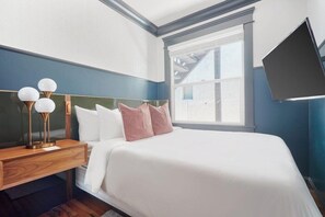 A bedroom with a bed, bedside table, lamp, and a TV mounted on the wall. - Sonder The Baker (San Diego)