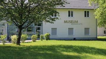 Een gebouw met een betegeld dak, aangeduid met 'MUSEUM WENDENER HÜTTE', omringd door gras en een boom.