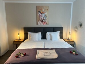 A neatly made bed with white linens, a dark headboard, and a decorative pillow. - Hotel Zum Landmann (Wenden)