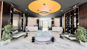 A modern lobby with a reception desk, seating areas, and a large circular light fixture.