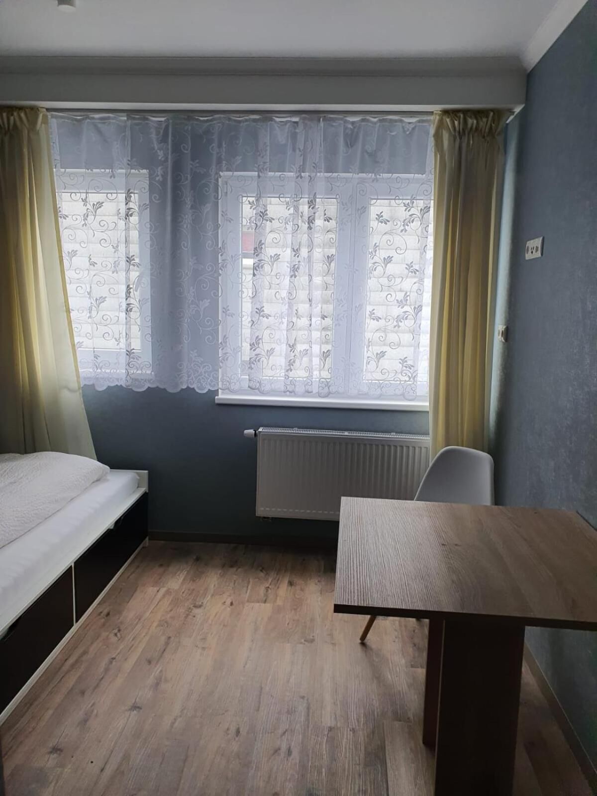 Ein Zimmer mit einem Bett, einem Tisch und einem Fenster mit Vorhängen.