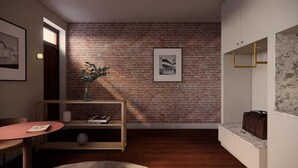A room with a brick wall, a framed picture, a small wooden shelf with books, a round table, and a marble bench. - Garde Hotel (Perth)