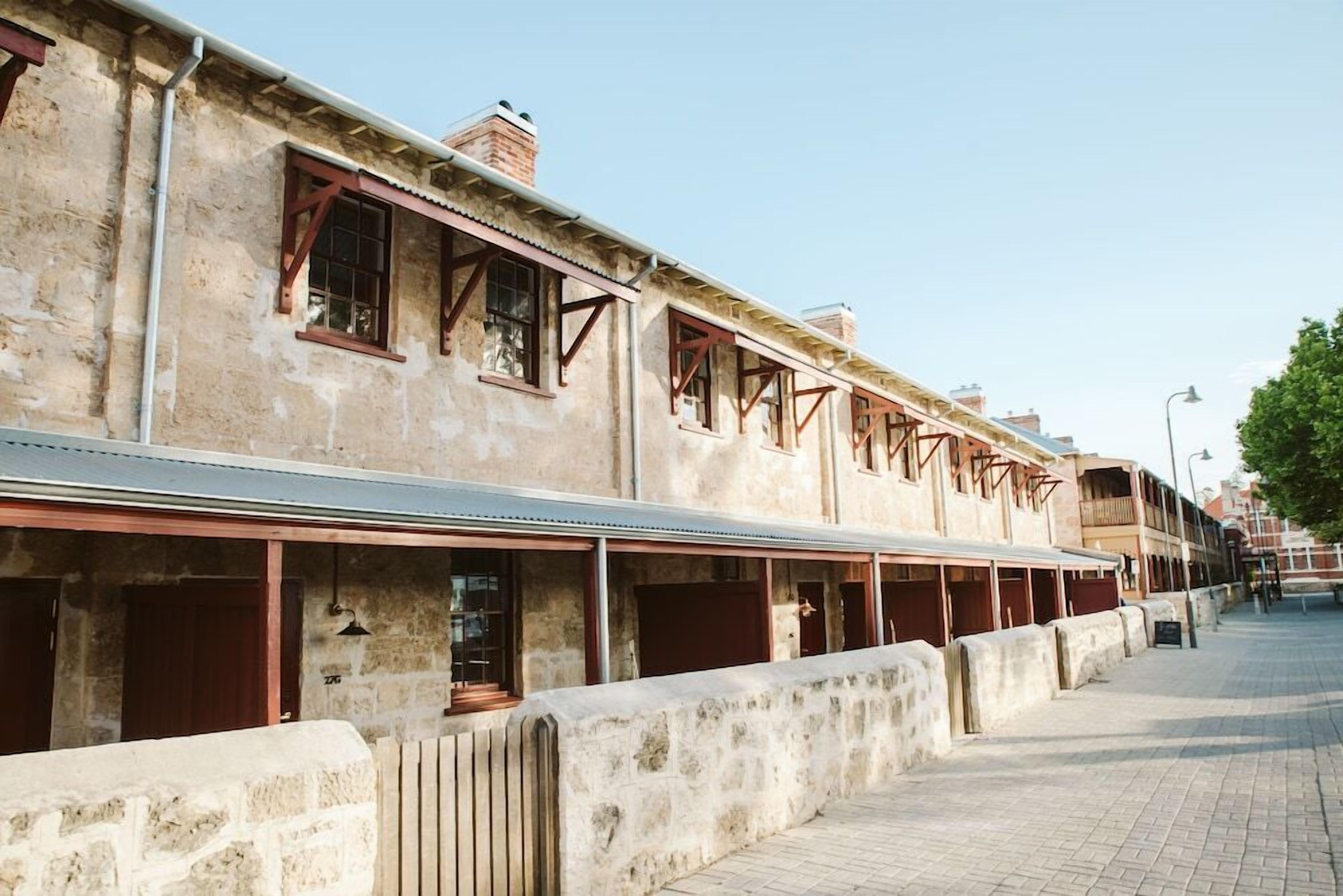 A row of stone buildings with multiple windows and doors, some with wooden shutters.