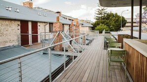 A rooftop terrace with a wooden deck, metal railings, and green chairs. - Garde Hotel (Perth)