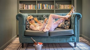 A teal sofa with a person reclining, a bookshelf in the background, and a bottle on the floor. - The House Hotel Galway (Galway)