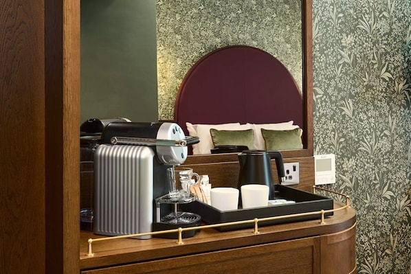 Ein Hotelzimmer mit Holzschreibtisch, einer Kaffeemaschine, einem Wasserkocher und einem Tablett mit Tassen und einem Glas.