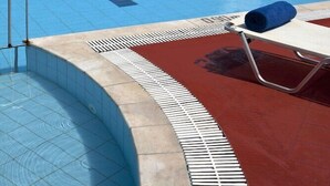 Ein Pool mit klarem, blauem Wasser, einer roten Liegefläche und ein Liegestuhl mit blauem Handtuch.
