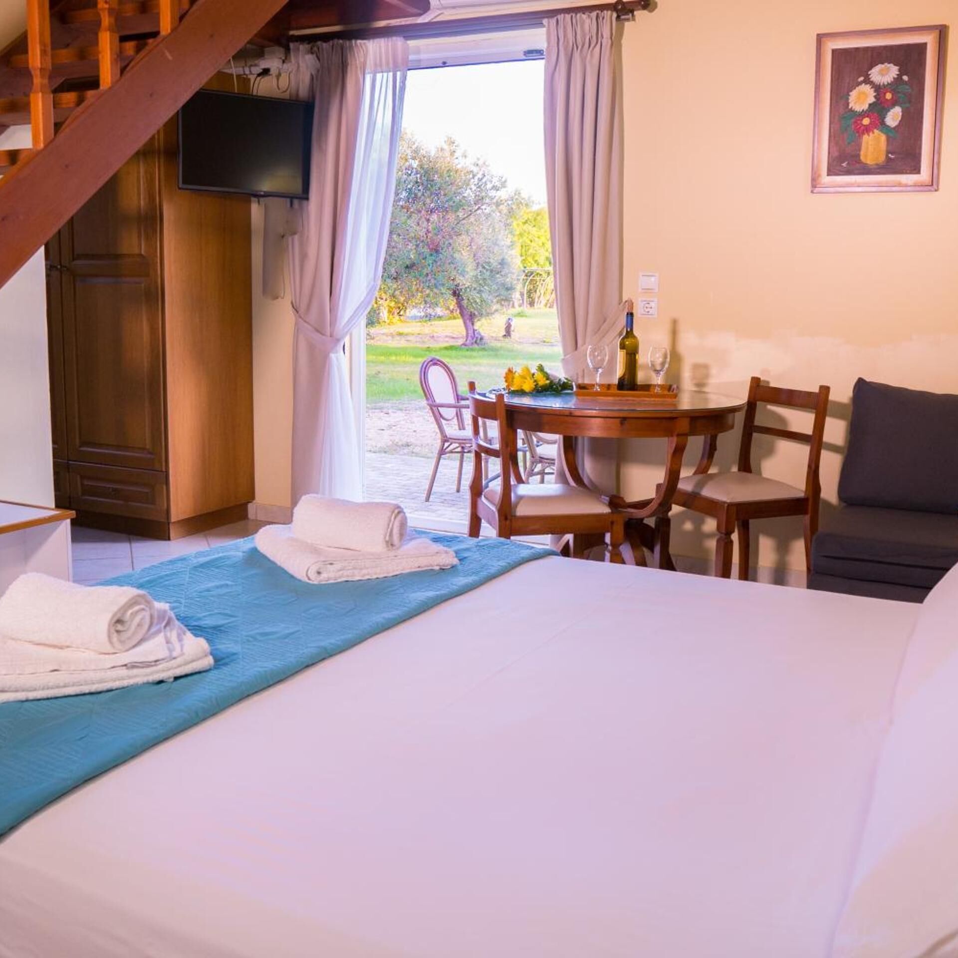 A hotel room with a bed, a dining table with chairs, a TV, and a view of the outdoors.