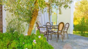 Eine Terrasse im Freien mit Tisch und Stühlen, umgeben von Grünpflanzen und einem Baum.