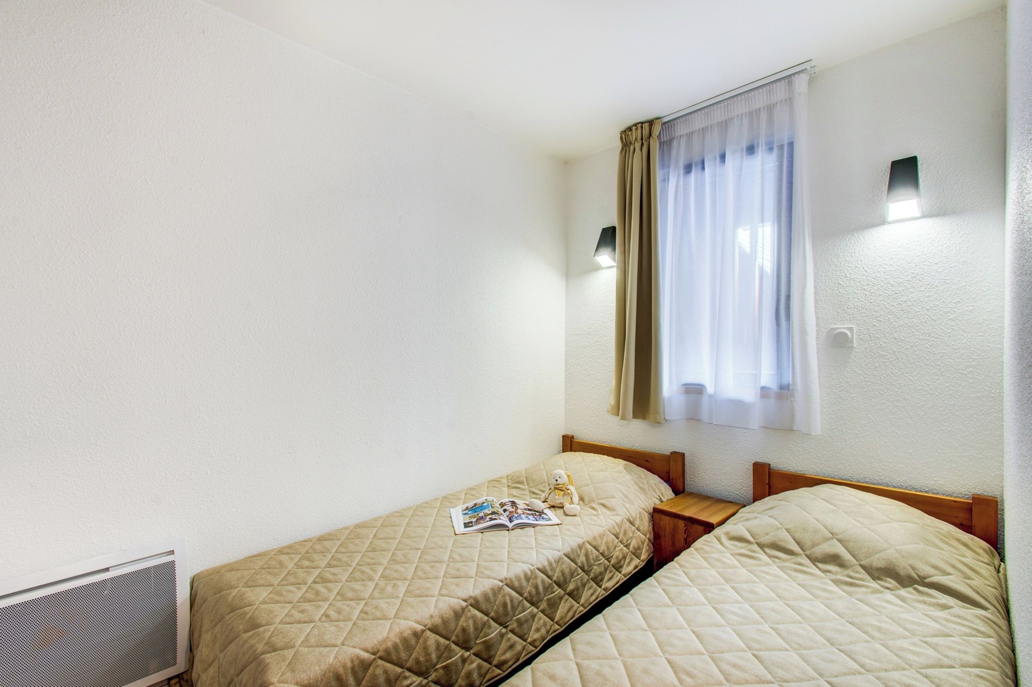 Habitación doble con dos camas, una ventana con cortinas, una lámpara de pared y un radiador.