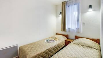 Habitación doble con dos camas, una ventana con cortinas, una lámpara de pared y un radiador.