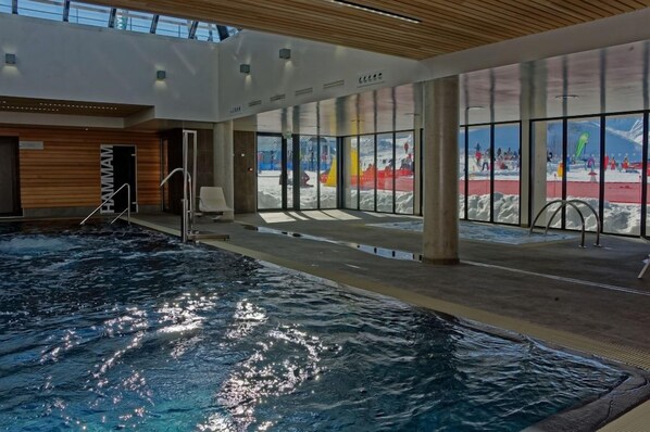 An indoor swimming pool with clear glass walls, a wooden ceiling, and a view of an outdoor snowy area.