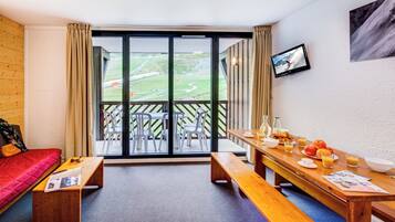 Una habitación con un sofá rojo, bancos de madera, una mesa de comedor con desayuno y vistas a un paisaje verde a través de amplios ventanales.