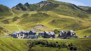 Un hotel con varias construcciones, ubicado en una zona montañosa con colinas verdes y cielos despejados.