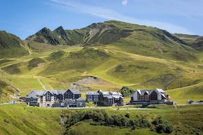 A hotel with multiple buildings, set in a mountainous area with green hills and clear skies.