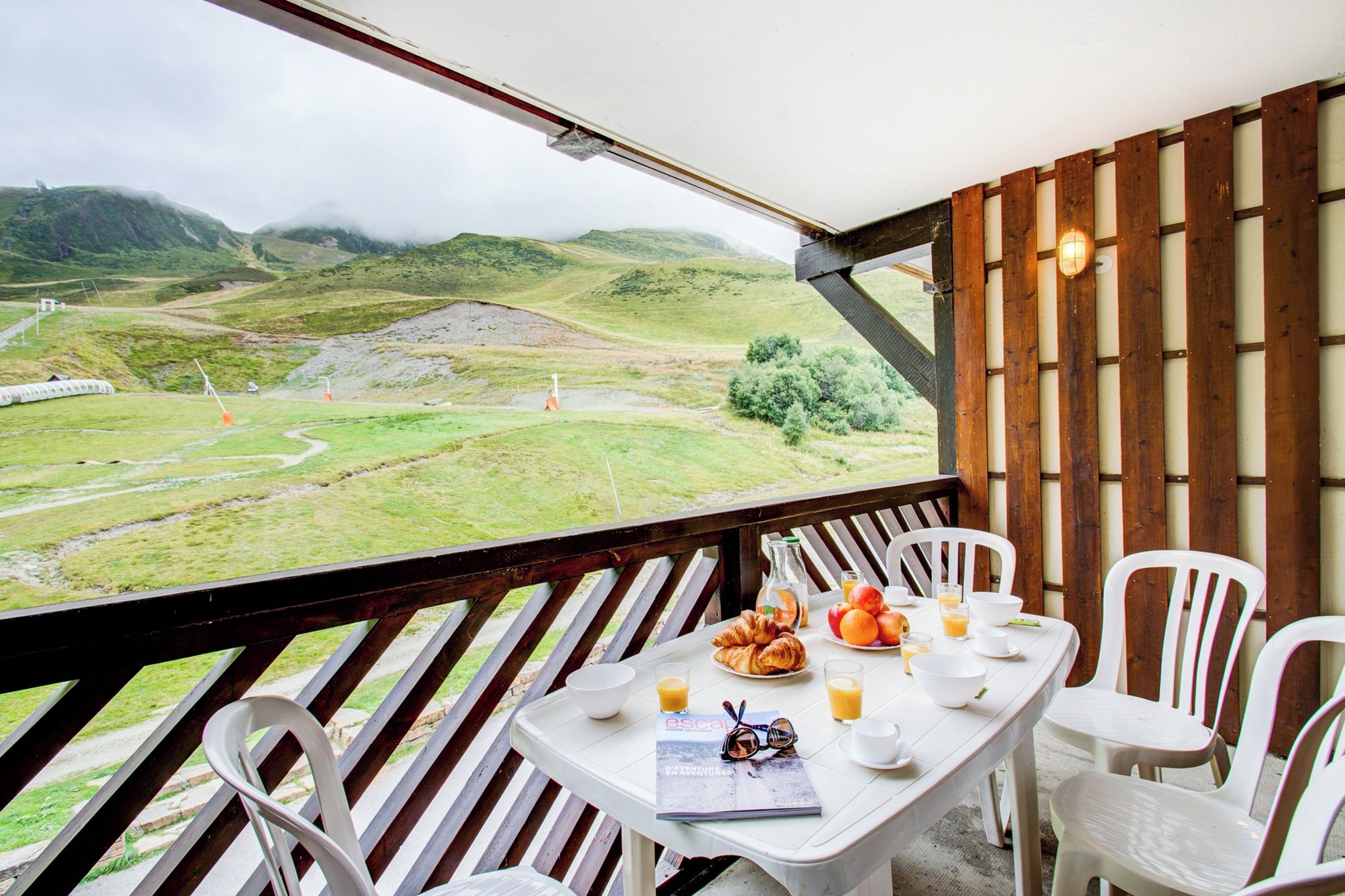 Una mesa con alimentos para el desayuno, sillas blancas y vistas a colinas verdes.