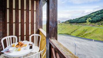 Un balcón con una mesa lista para el desayuno, con vistas a una carretera y colinas verdes.