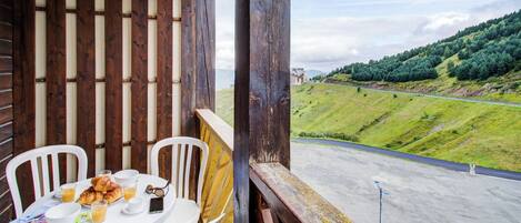 A balcony with a table set for breakfast, overlooking a road and green hills.