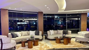 A modern living room with sofas, coffee tables, and a large window offering a city view. - XU San Stefano Hotel Alexandria (Alexandria)