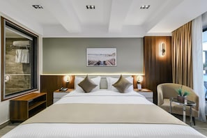 Quarto de hotel moderno com uma cama grande, mesa de cabeceira, espelho, quadro pendurado na parede e janela com cortinas.