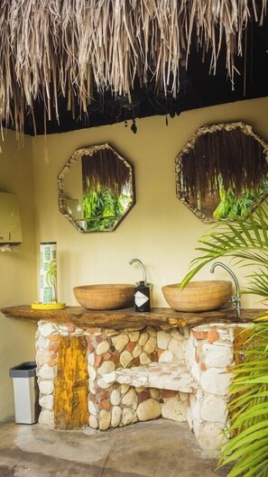 A bathroom with a stone sink, two mirrors, a thatched roof, and a potted plant. - Santuario Beach Hostel (Cartagena)