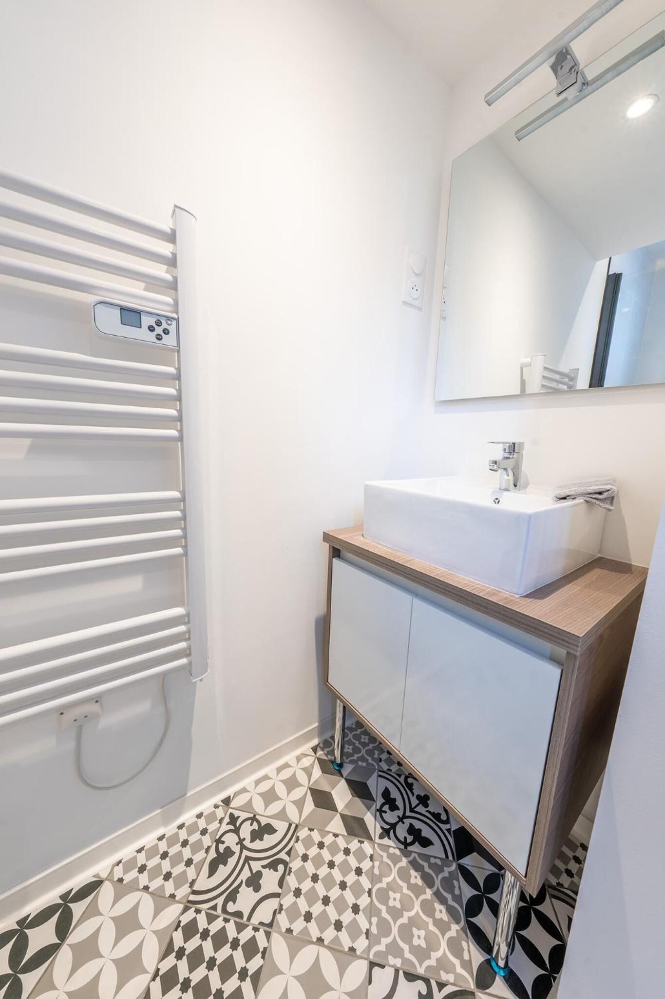 Une salle de bain moderne avec un lavabo blanc, un miroir et des carreaux de sol à motifs.