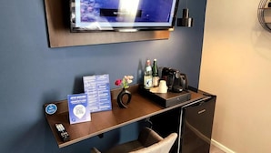 Una habitación de hotel moderna con un televisor montado, un escritorio con silla, un minibar y una pequeña zona de estar.