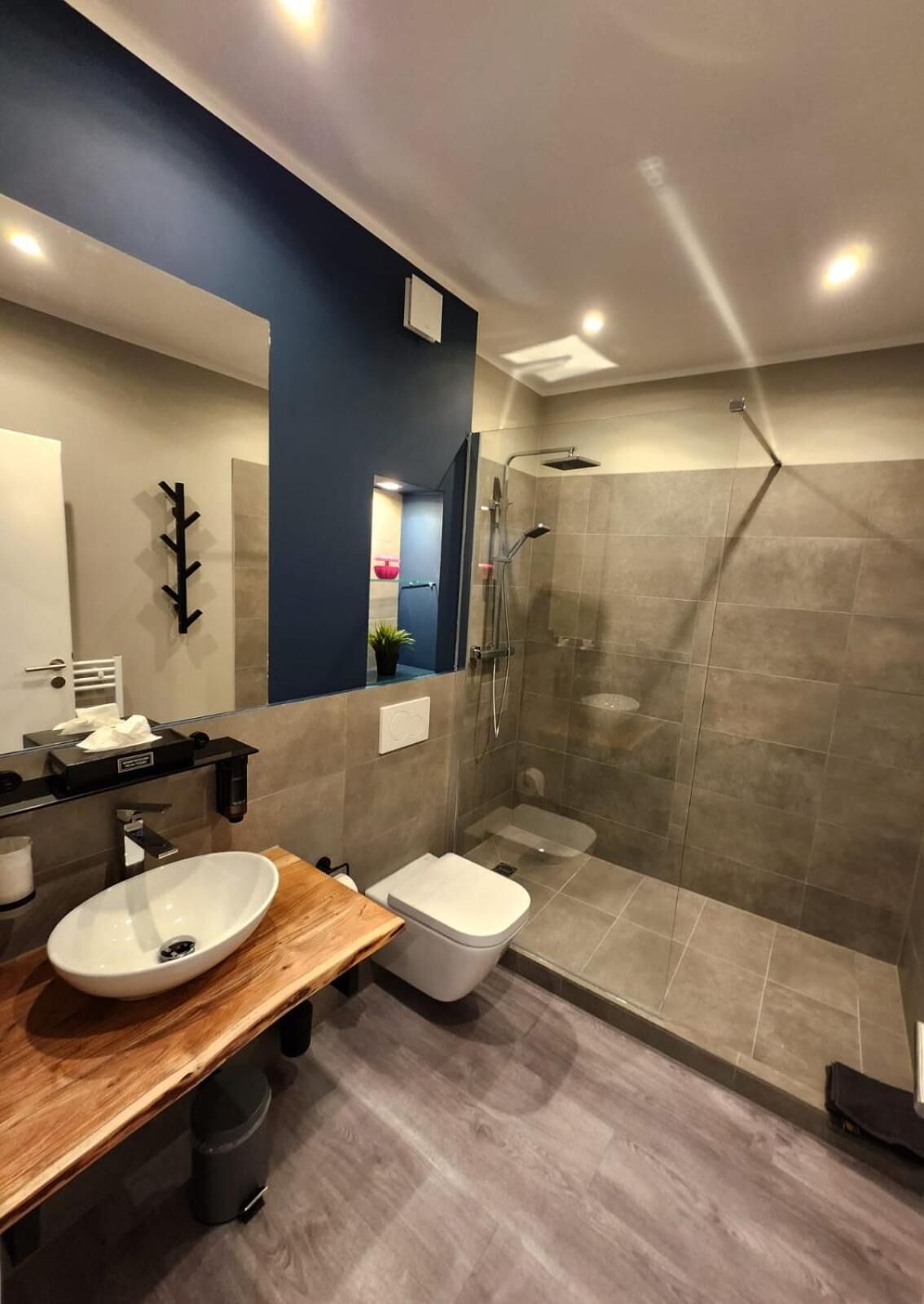 Une salle de bain moderne avec un meuble-lavabo en bois, un lavabo blanc, des toilettes et une douche à parois de verre.