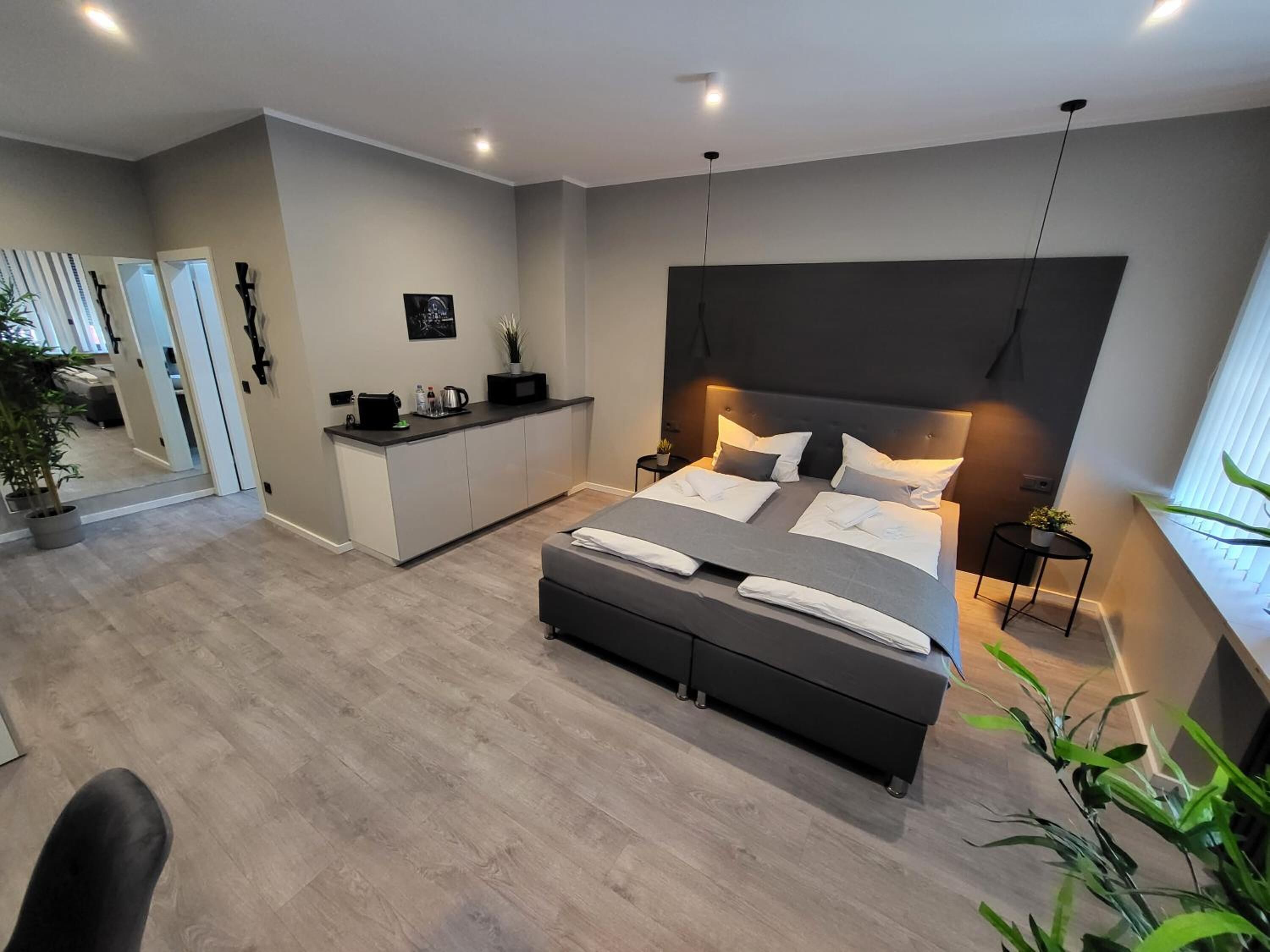 Une chambre moderne avec un grand lit, des tables de chevet, un petit bureau et une fenêtre avec des stores.