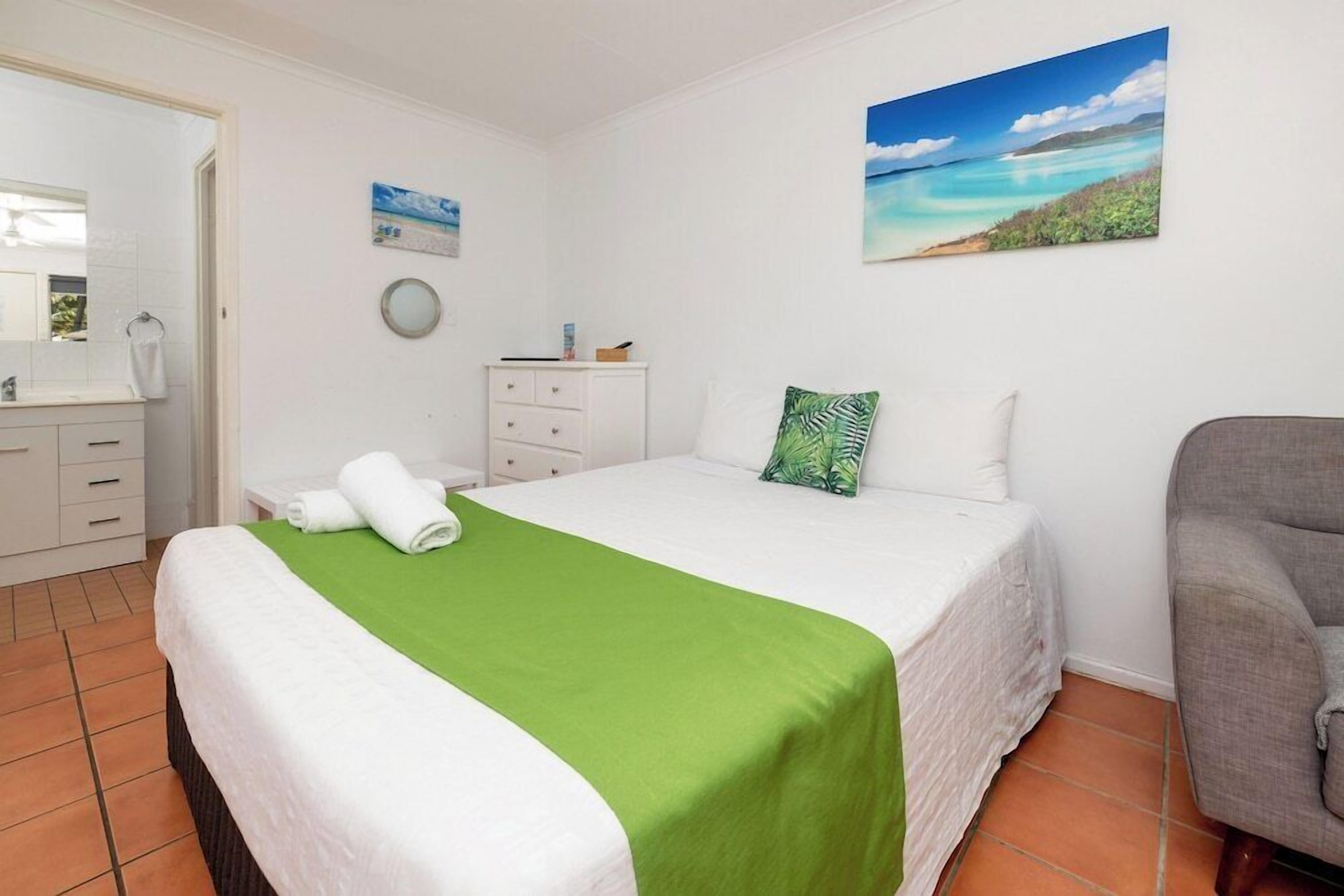 A hotel room with a bed, a chair, a dresser, and a painting of a beach scene.