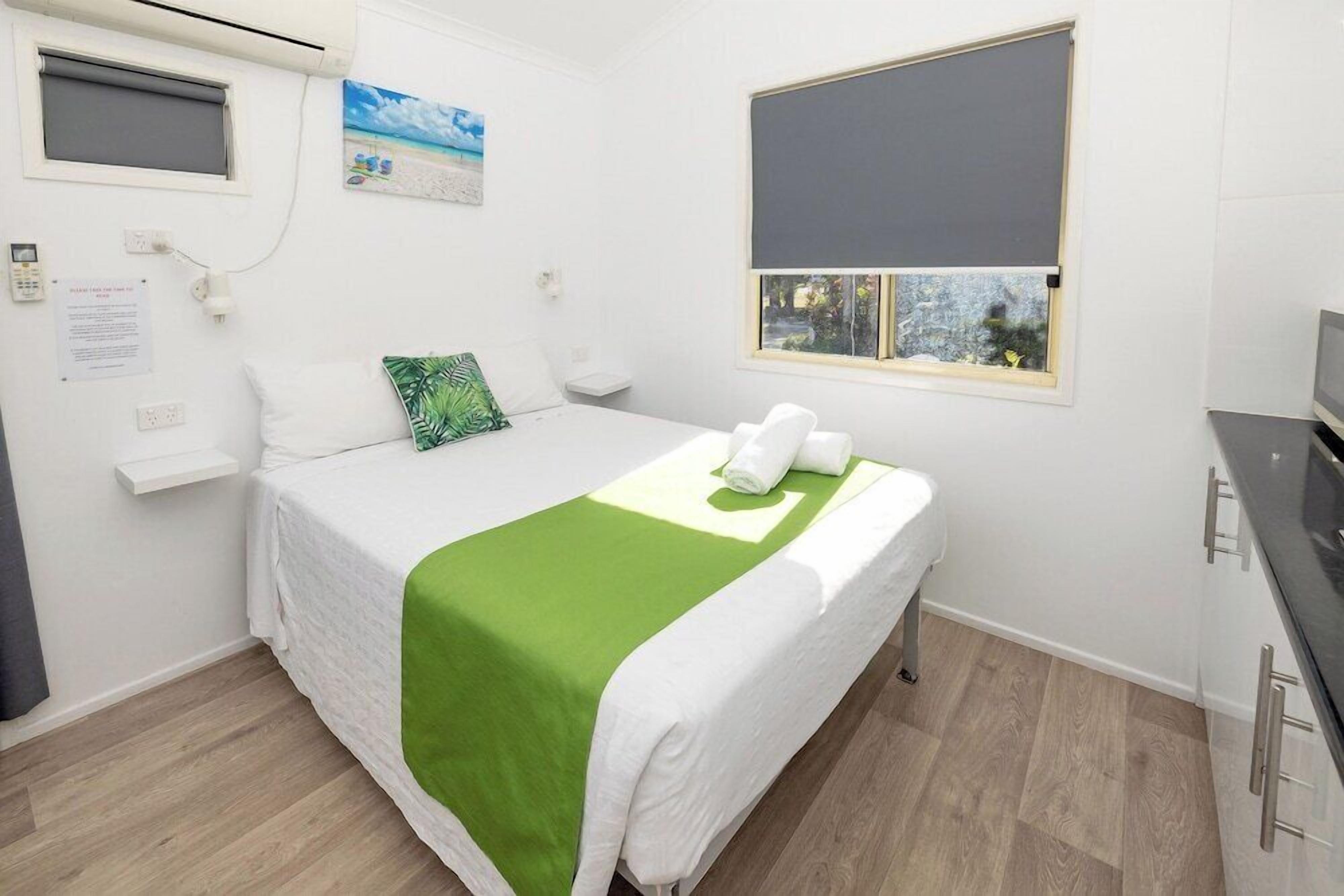Ein Hotelzimmer mit Bett, einem Fenster mit Blick, einem kleinen Nachttisch und einer Wand-Klimaanlage.
