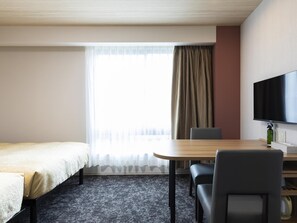Een hotelkamer met een bed, een bureau, een stoel, een televisietoestel en een raam met gordijnen.